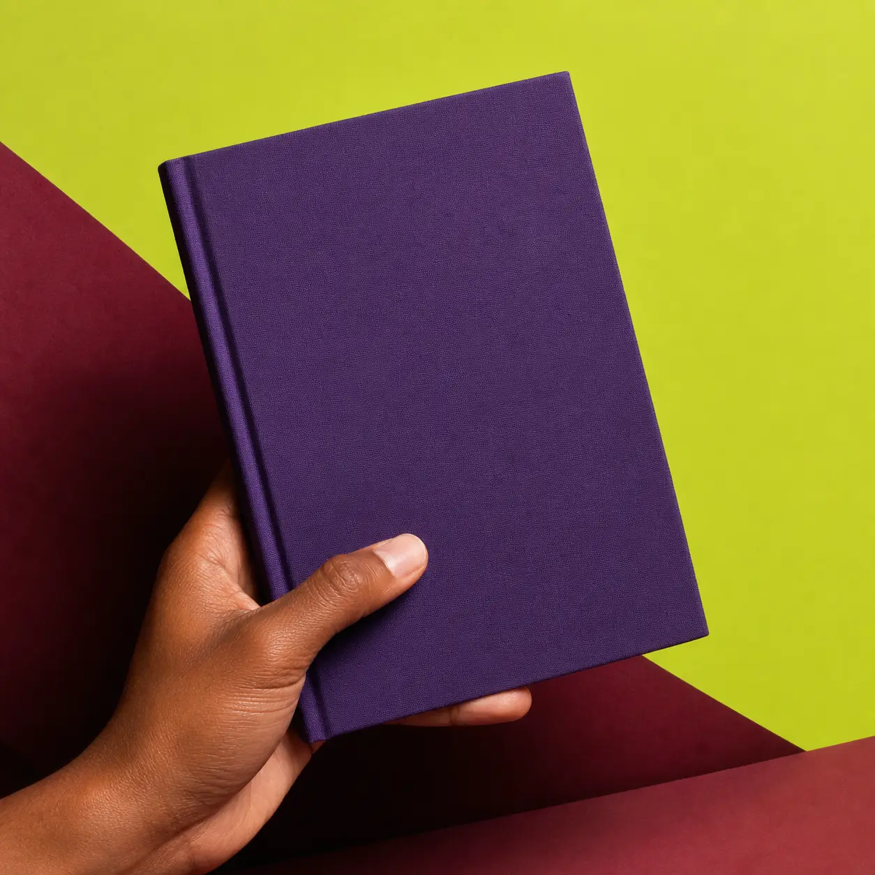 Une main tient un carnet violet sans marque sur un décor graphique.